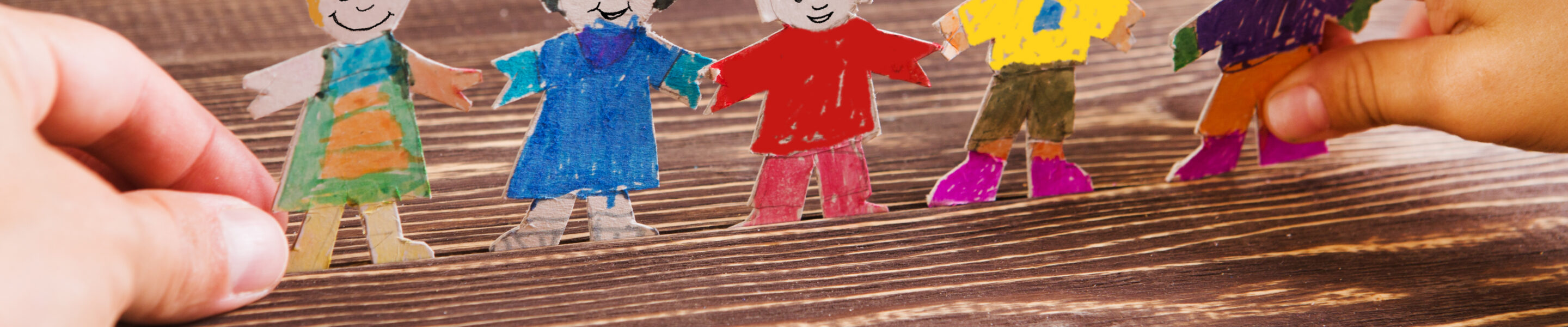 the child does figures of people of paper. Paper people on wooden background. Creative child play with craft.