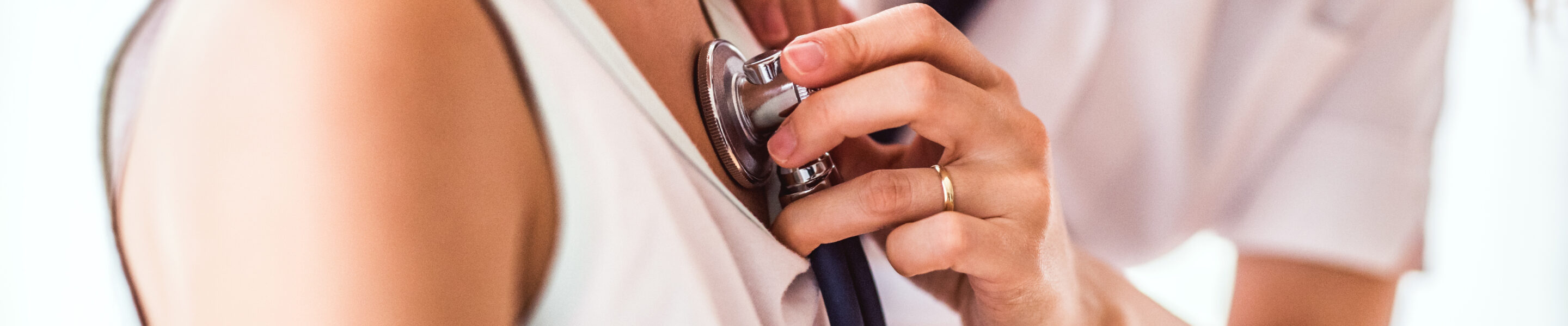 Unrecognizable young female doctor examining a small girl with stethoscope in her office. Close up.