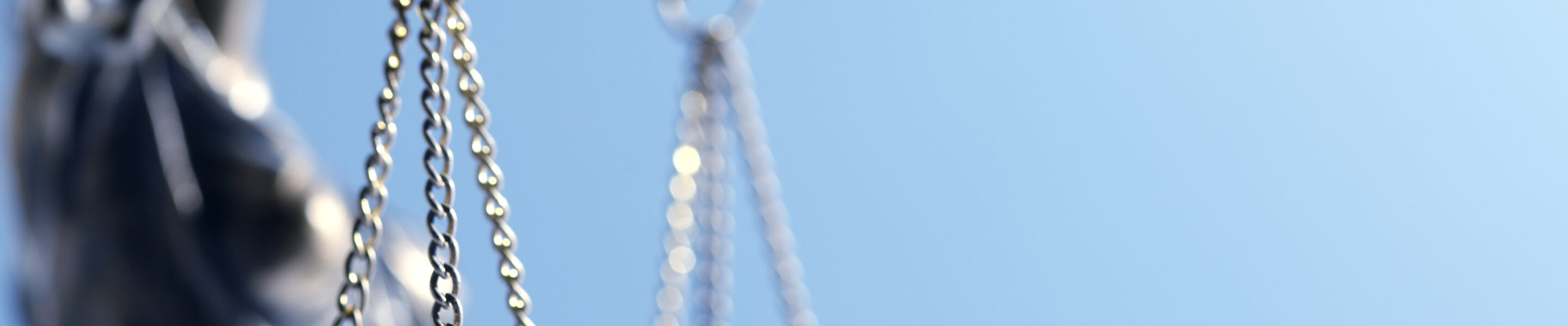 A close up and a low angle view of a statue of lady justice as it sits in front of a blue background The image is photographed with a very shallow depth of field with the focus being on the justice scale.