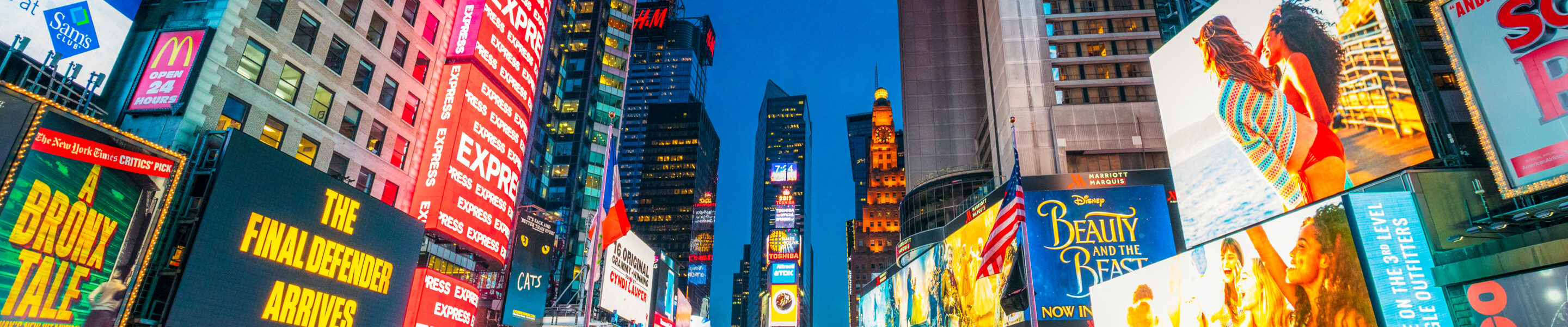 Times Square covered with illuminated billboards during the 'blue hour' period at dusk, with tourists on the streets.