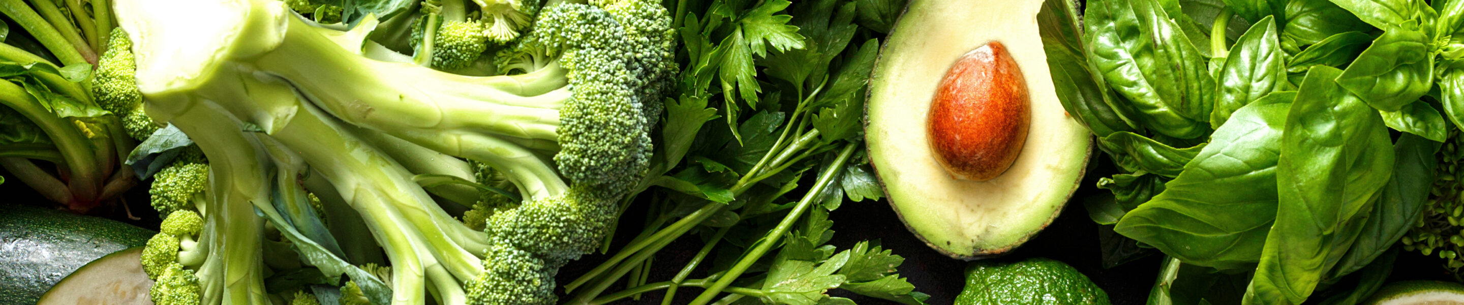 Raw healthy food clean eating vegetables: cucumber, alfalfa, zucchini, spinach, basil, green peas, dill, parsley, avocado, broccoli, lime on dark stone background, top view