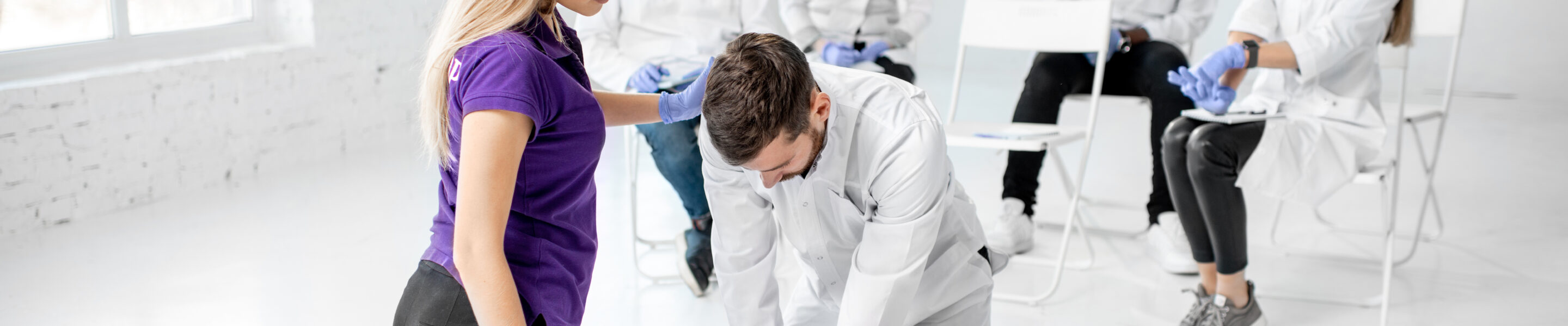 Group of young medics practising to make artificial breathing with medical dummies during the first aid training in the white room