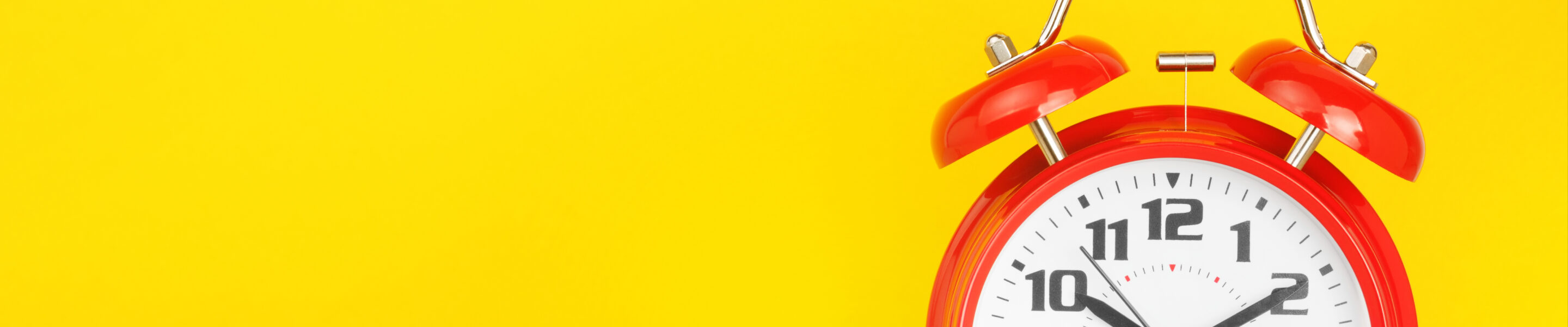Red alarm clock and glasses on a wooden table against a yellow background. The concept of time, delay, morning rise, reading, poor eyesight. Layout with copy space for your text.