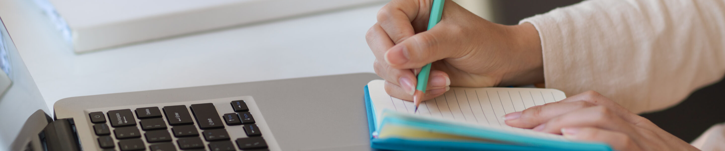Side view of female hand writing on notebook while working with laptop on the table in office room