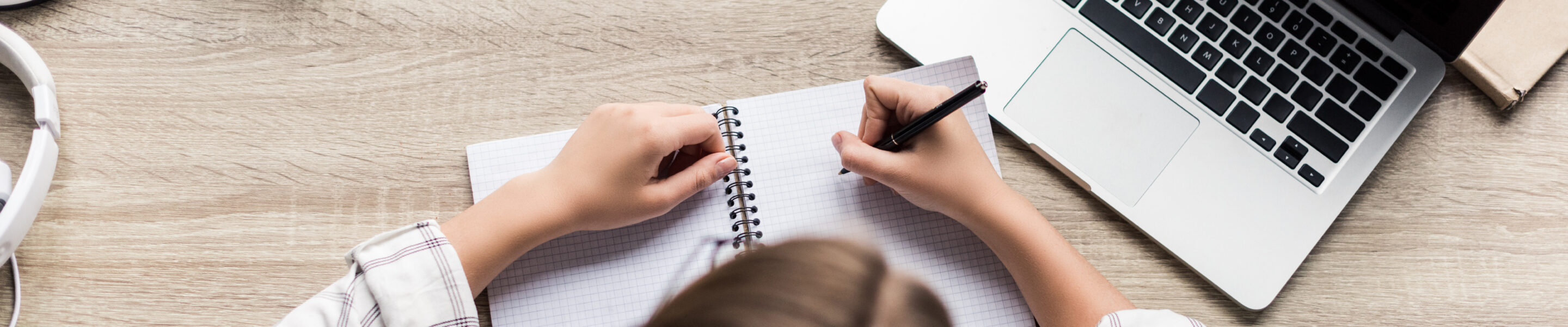 top view of young woman writing in notebook at workplace