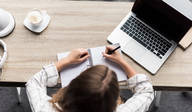 top view of young woman writing in notebook at workplace