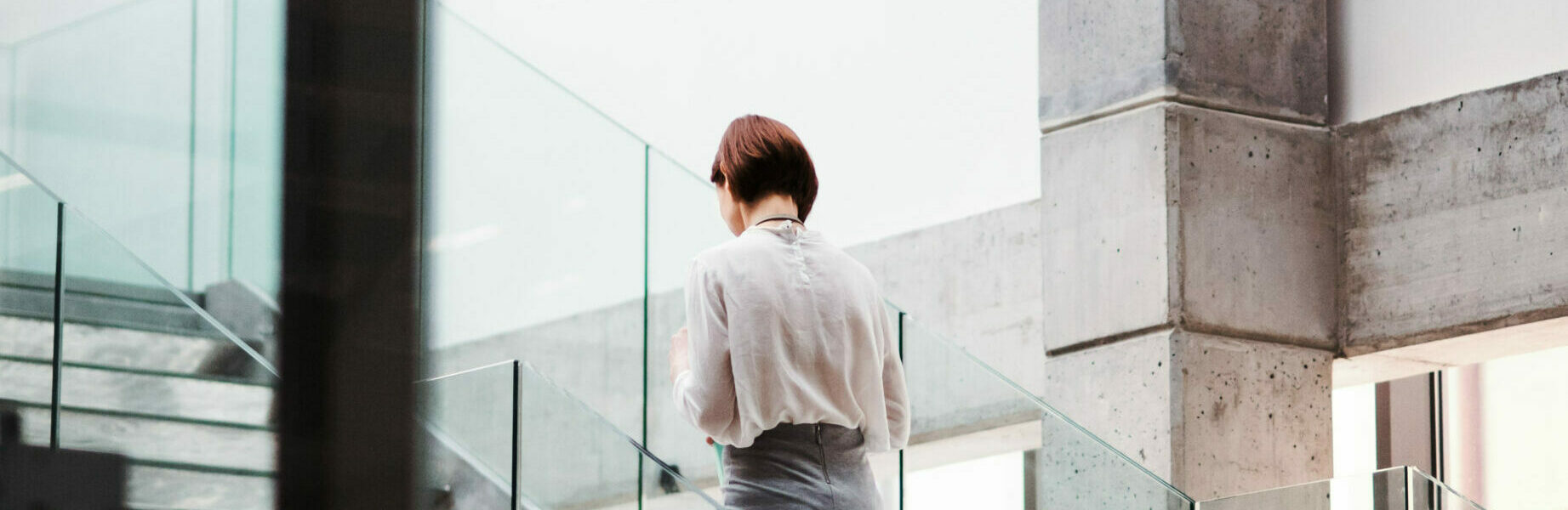 A rear view of young businesswoman walking up the stairs in office building. Copy space.