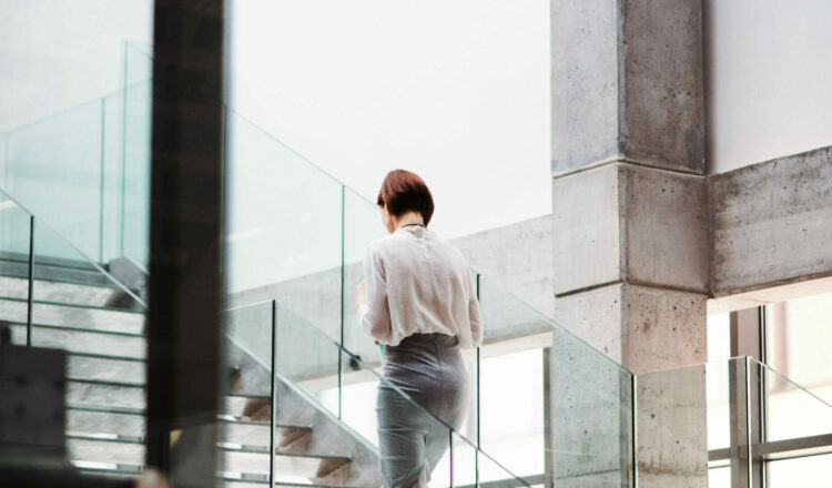 A rear view of young businesswoman walking up the stairs in office building. Copy space.